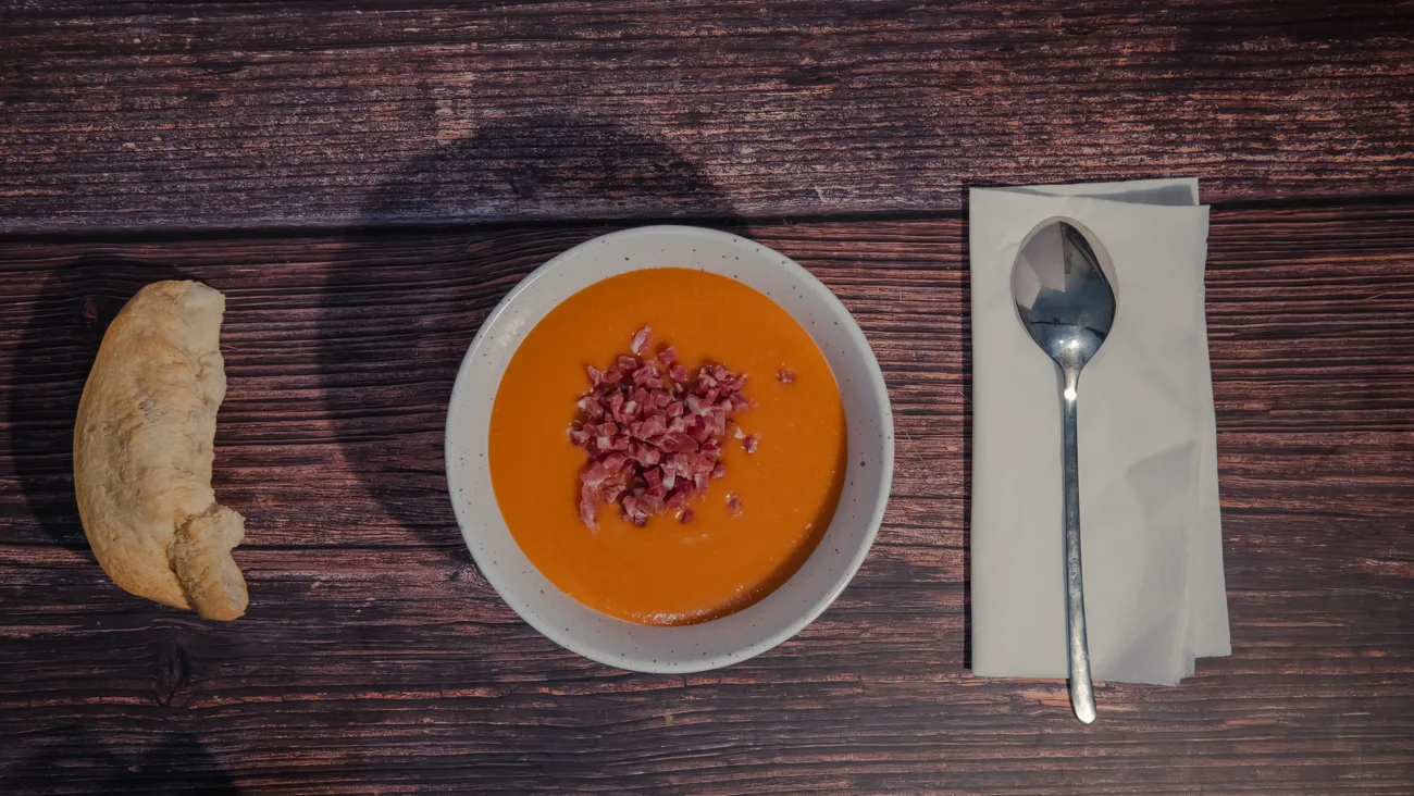 Composición de salmorejo, pan y cuchara sobre una mesa rústica
