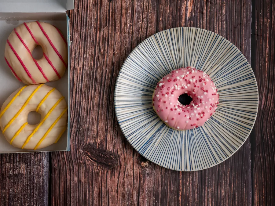 Donut de cobertura rosa con pequeñas decoraciones blancas y rosas