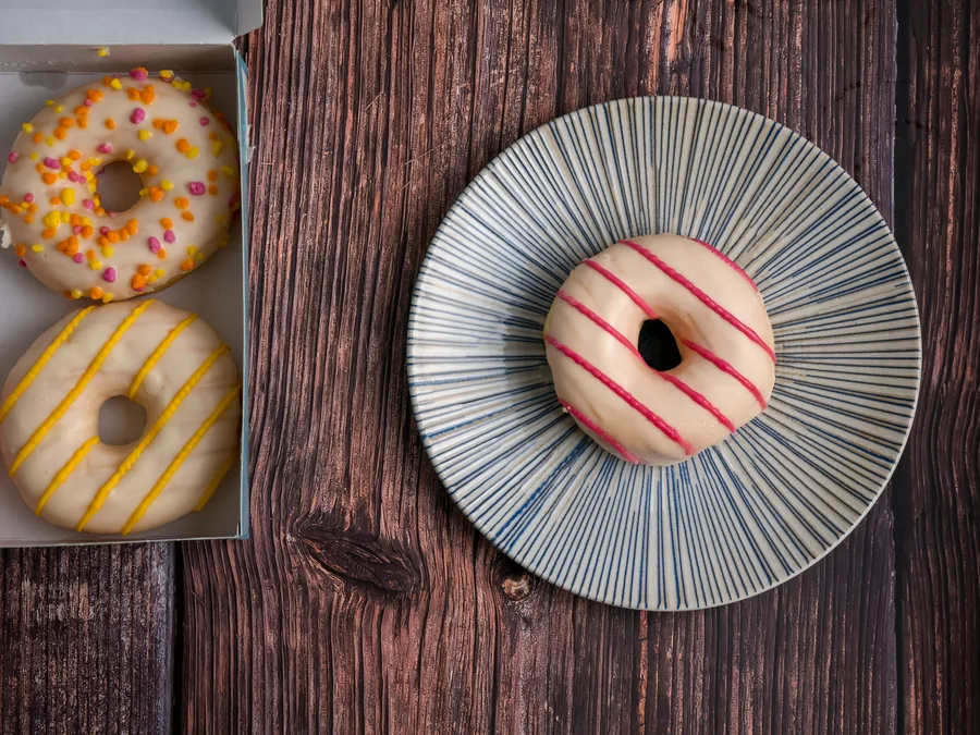 Donut de cobertura blanca con líneas rosas junto a una caja de donuts