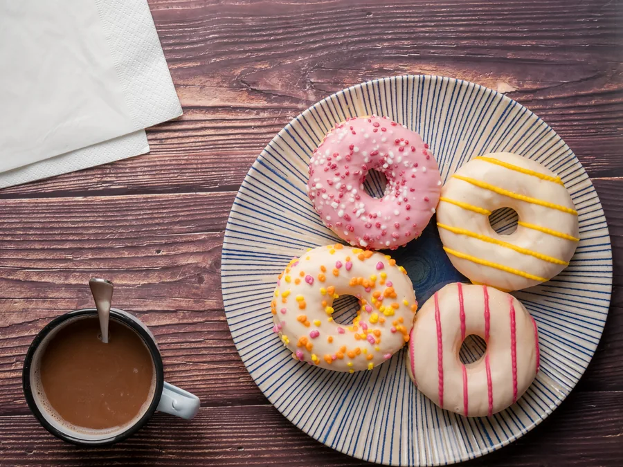 Cuatro donuts decorados en un plato de rayas junto a una taza de café