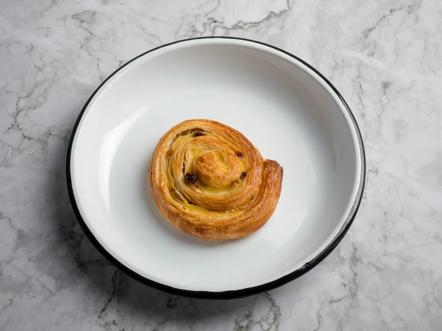 Espiral de hojaldre con pasas en un plato blanco sobre mármol