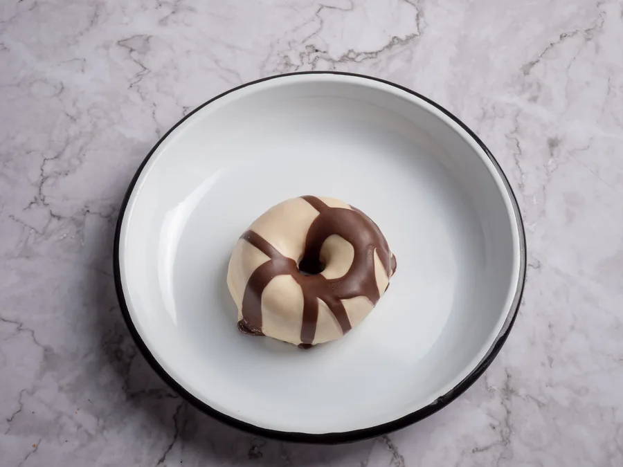 Donut con cobertura de chocolate blanco y chocolate con leche en un plato blanco