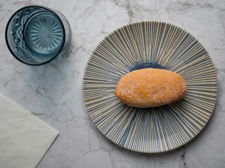 Bollo ovalado cubierto de azúcar en un plato de rayas azules