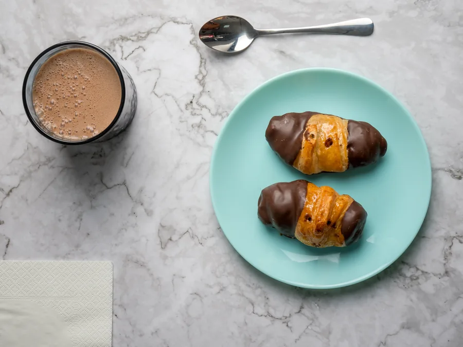 Dos pequeños cruasanes bañados en chocolate sobre un plato turquesa