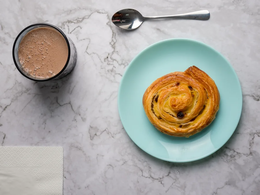Espiral de hojaldre con pasas en plato turquesa junto a una bebida de chocolate