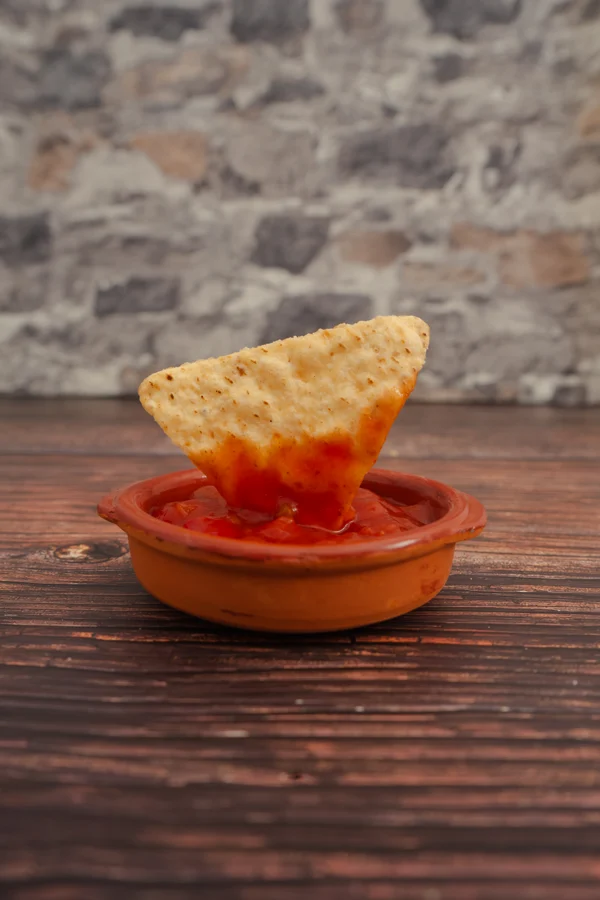 Nacho sumergido en salsa roja en una cazuela de barro