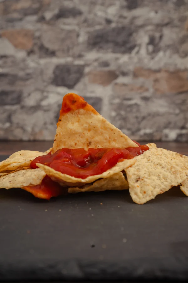 Nacho inclinado con salsa roja sobre una bandeja de nachos