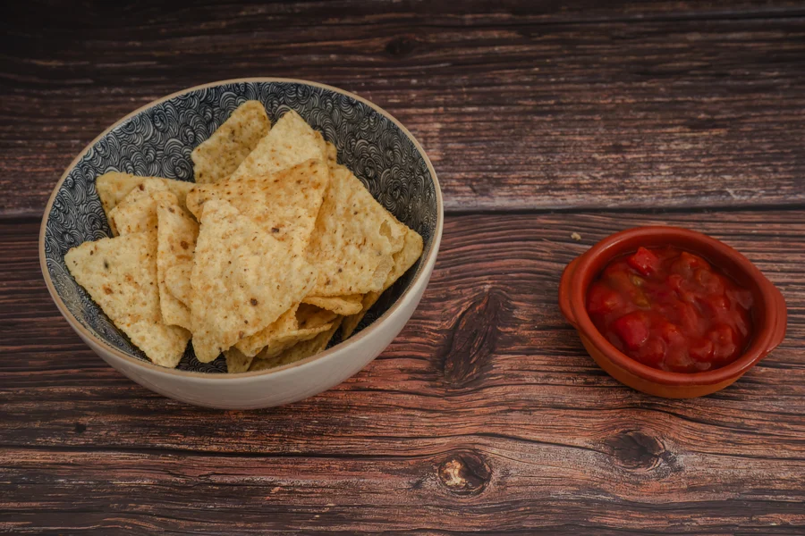 Cuenco de nachos junto a una cazuela de salsa roja sobre madera