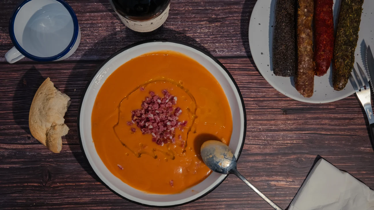 Salmorejo y bocados sobre una mesa de madera, vistos desde arriba