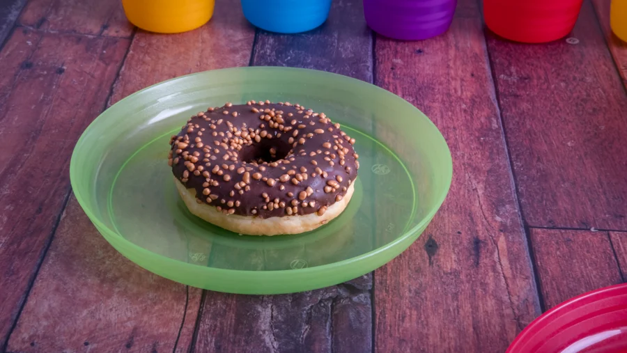 Rosquilla de chocolate en plato verde con vasos de colores