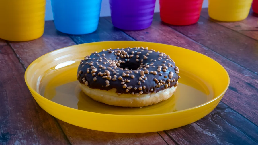Rosquilla de chocolate sobre plato amarillo con vasos al fondo
