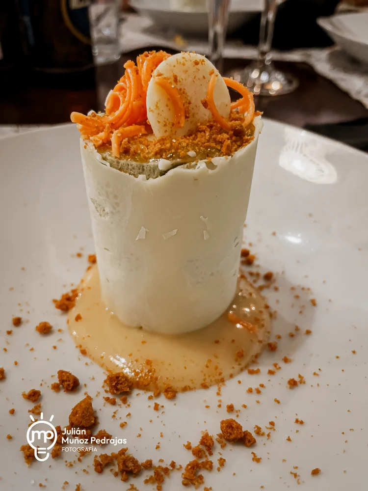 Postre de forma cilíndrica con cobertura blanca, helado y migas crujientes