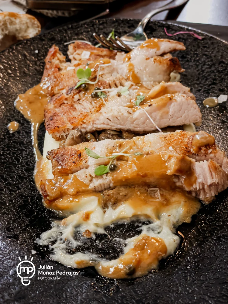 Carne con salsa y guarnición sobre un plato negro de textura rugosa