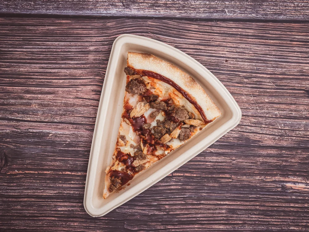 Porción de pizza con carne y salsa en un plato triangular sobre madera