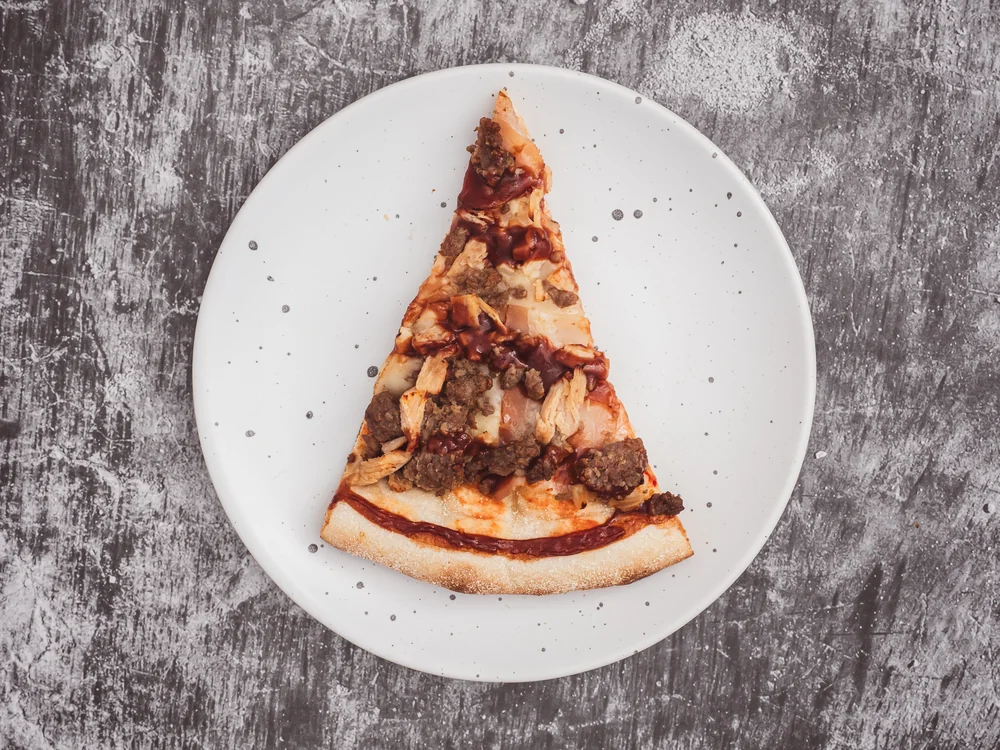 Porción de pizza en un plato blanco sobre fondo gris